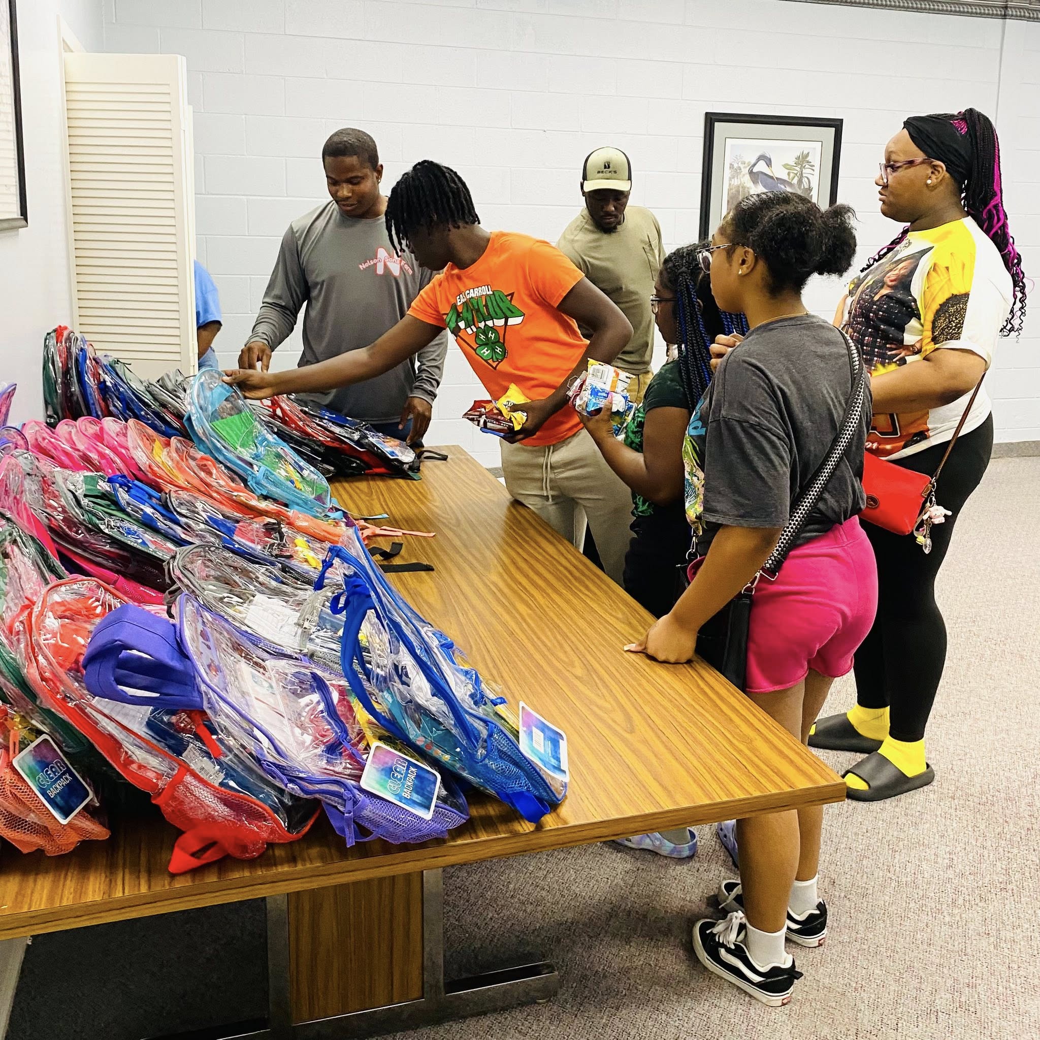 A group of teenagers looking at a stack of backpacks on a table.